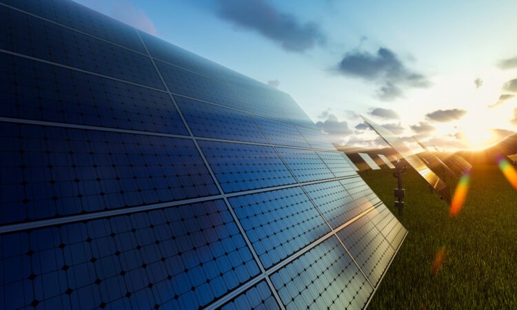 A solar panel up close with the sun rising in the distance.