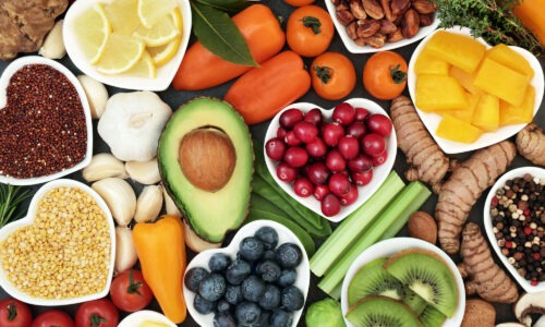 A close up of foods rich in colour. Showing various seeds, cut up melon, berries, kiwi, peppers and garlic.