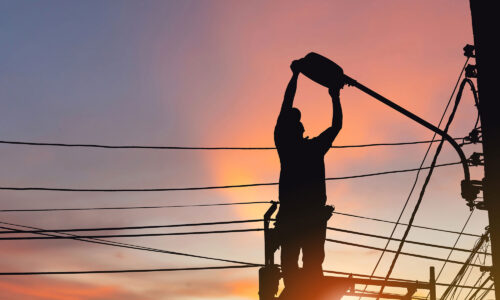 A sunset, with a man on scaffolding fixing a street light. The figure is in silhouette.