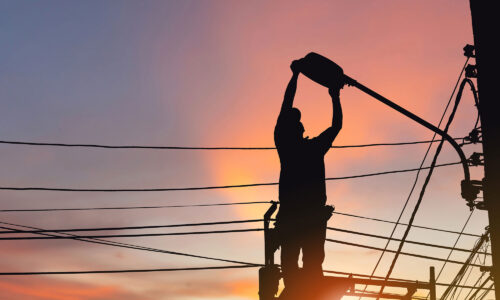 A sunset, with a man on scaffolding fixing a street light. The figure is in silhouette.