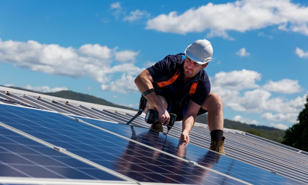 Image shows a workman on top of roof top solar panels.