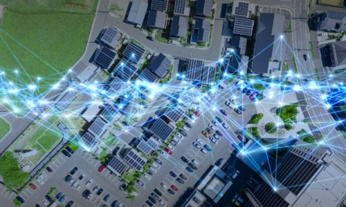An aerial view of a car park and buildings, lots of buildings have solar panels on their roofs. You can also see a green field to the left and a lot of cars parked in various spaces. Over the top of this are what look like laser beams of blue joining together.