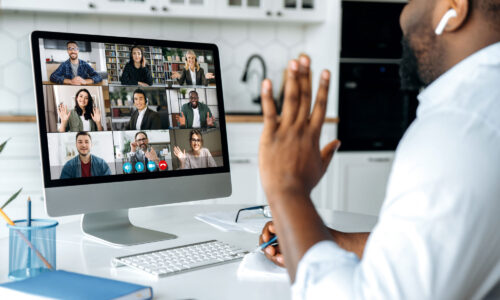 A black male working from home on a video call with his colleagues appearing on the screen.
