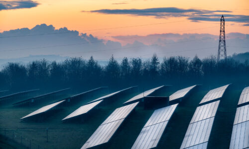 Images shows a sunset with hills in the background and a solar farm in the foregroun