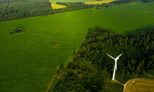 Image shows an open green landscape, birds eye view with a wind turbine in the bottom right corner